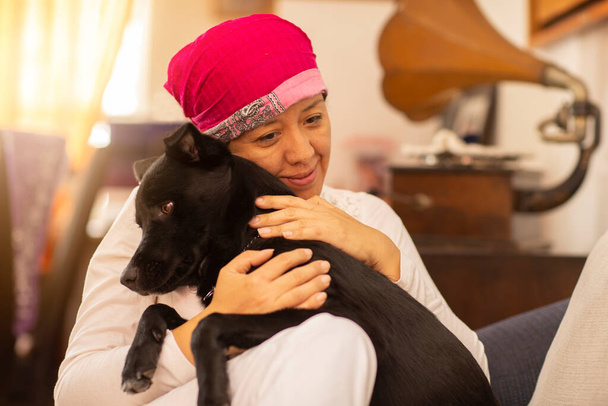 vrouw knuffelen haar huisdier, en met roze sjaal op haar hoofd als gevolg van borstkanker - Foto, afbeelding