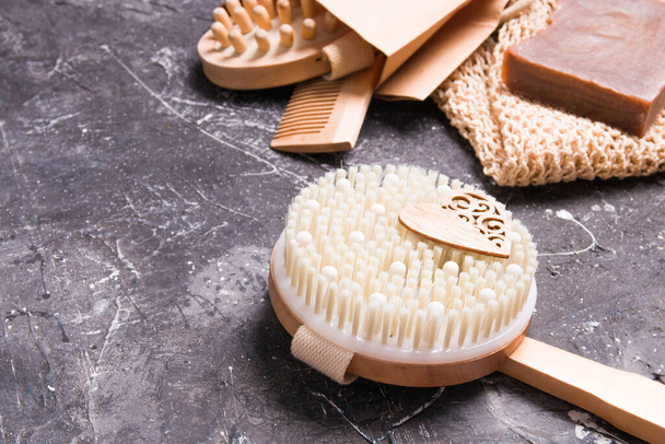 round wooden brush for dry massage against cellulite on a black background, eco friendly lifestyle, home soap, knitted washcloth, wooden comb in the background - Foto, imagen