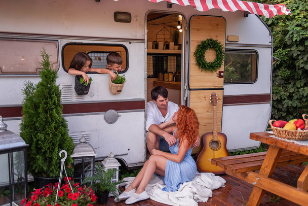 Happy cheerful beautiful family are sitting resting near their trailer truck. Travel concept with picnics. Mother, father, son, daughter spend time together going on a camping trip. Rest on nature - Foto, imagen