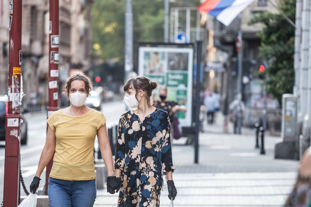 BELGRADE, SERBIA - 6 GIUGNO 2020: Giovani, due giovani amiche, che camminano tenendosi per mano indossando maschere protettive e guanti latext su Coronavirus Covid 19 crisi - Foto, immagini
