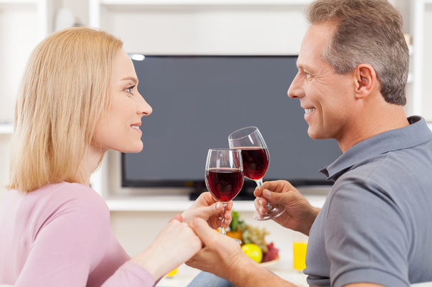 Couple sitting in front of TV and holding glasses with red wine - Photo, image