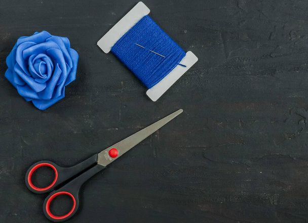 A scissor, a spool of blue wool threads and a blue rose lie in the upper left corner and with space for text in the lower right corner, close-up top view. - Photo, Image