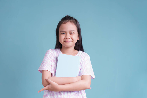 happy Asian little girl standing holding the book  on blue background isolated - Fotó, kép