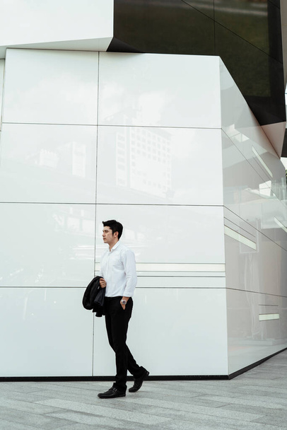 Mature asian business man on white formal shirt holding suit on arm walking at white wall. - Fotoğraf, Görsel