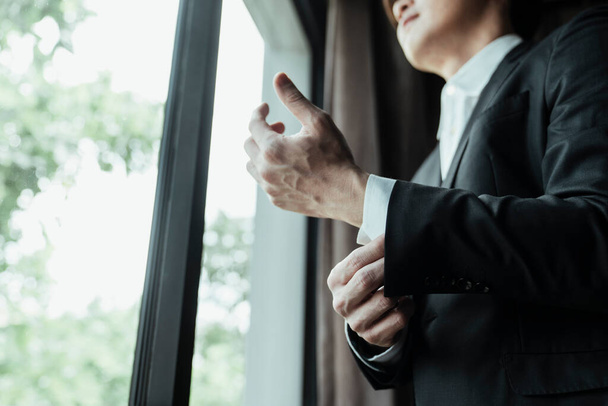 Mano de empresario asiático vestido traje negro cerca de la ventana. Enfocado en la mano y mangas
.  - Foto, Imagen