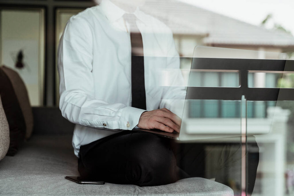 Uomo d'affari su camicia bianca seduto su un divano utilizzando il computer portatile in casa. - Foto, immagini