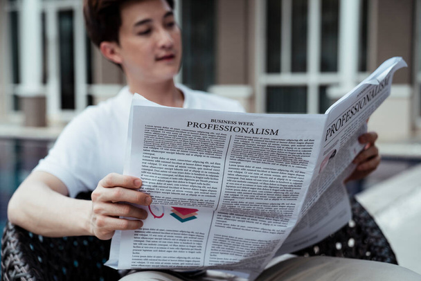 Asijské bohatý chlap obchodník čtení zpravodajství papír v resort sedí na židli v blízkosti bazénu. - Fotografie, Obrázek