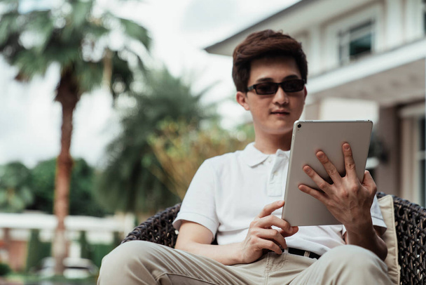 asiatico ragazzo su bianco camicia utilizzando tablet all'aperto a casa zona. - Foto, immagini