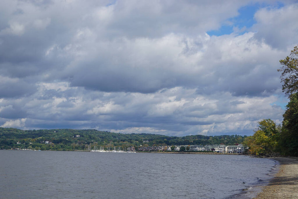 Croton-On-Hudson, New York, USA: Pohled na domy a přístav na řece Hudson pod oblačnou oblohou, z oblázkové pláže v Croton Point Park. - Fotografie, Obrázek