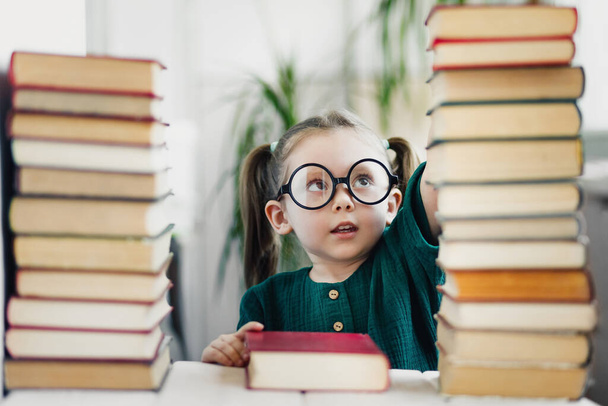 小さな就学前のかわいい女の子の天才は多くの本を読んでいます。子供の教育と早期開発の概念. - 写真・画像