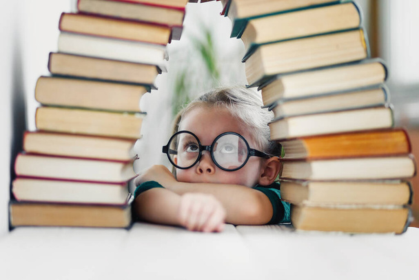 Niña cansada en edad preescolar mirando pilas de libros, demasiado concepto de lectura y educación
 - Foto, Imagen