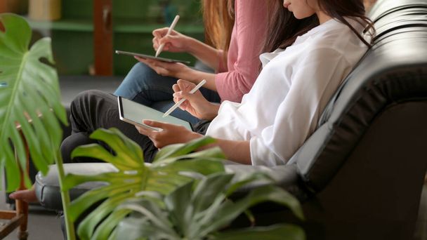 Siyahi kanepede oturan ve oturma odasında Stylus 'lu dijital tabletler kullanan kadın üniversite öğrencilerinin yan görüntüsü.  - Fotoğraf, Görsel