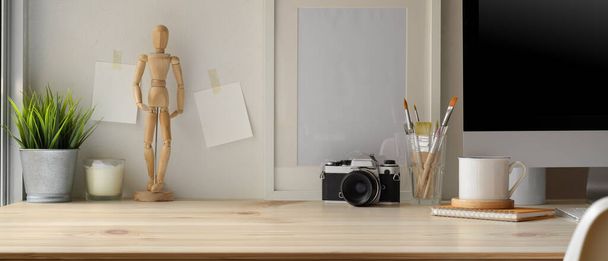 Vista de perto do escritório doméstico moderno com computador, câmera, pincéis de pintura, suprimentos, decorações e espaço de cópia na mesa de madeira
 - Foto, Imagem