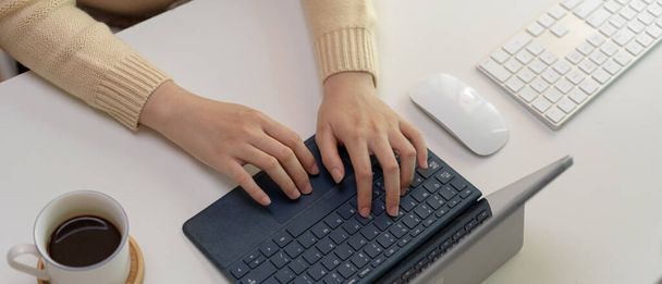 Oříznutý záběr zaměstnankyně psaní na digitální klávesnici tabletu na bílém kancelářském stole s šálkem kávy a počítačovými přístroji - Fotografie, Obrázek