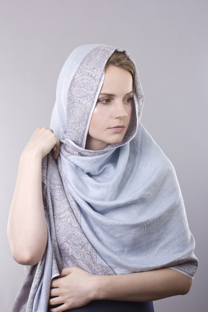 Hermosa joven rubia en una bufanda azul pálido en su cabeza sobre fondo gris
 - Foto, imagen