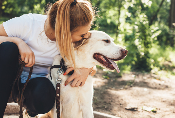 Close up photo of a caucasian woman and her golden retriever embracing in the park in a sunny summer day - Photo, Image