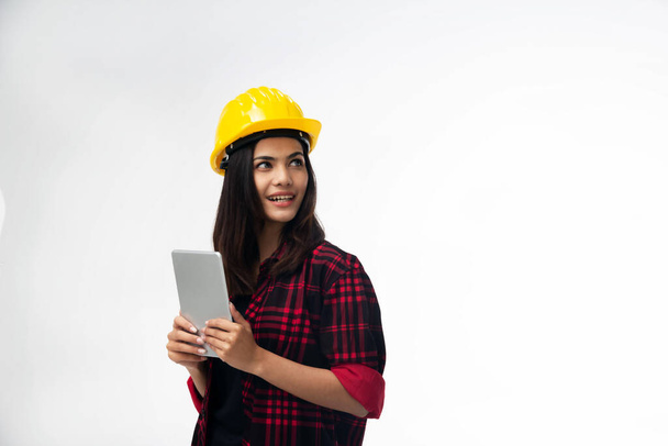De jonge vrouw ingenieur met gele veiligheidshelm met taplet in de hand, kleine glimlach en draai gezicht naar links voor looikng iets - Foto, afbeelding