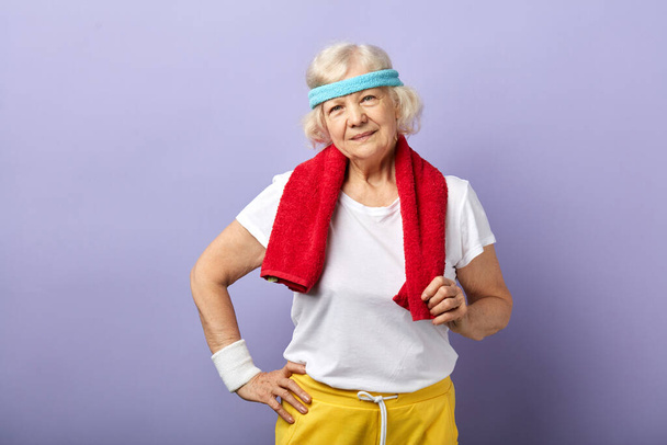 Elderly sportswoman with headband and red towel on neck, looking at camera - Foto, Imagen
