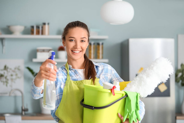 Jonge vrouw met schoonmaak benodigdheden in de keuken - Foto, afbeelding