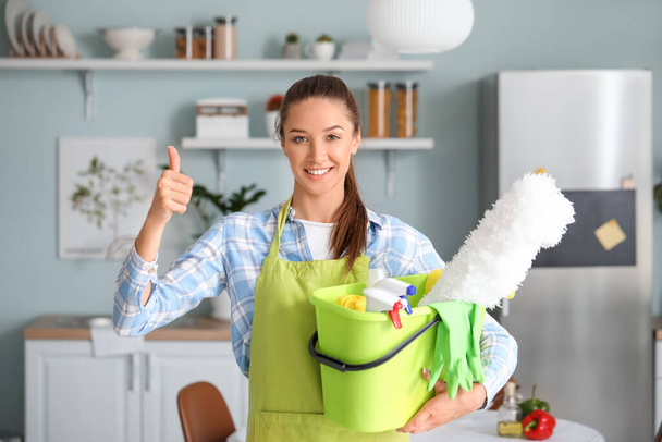 Jonge vrouw met schoonmaak benodigdheden in de keuken - Foto, afbeelding