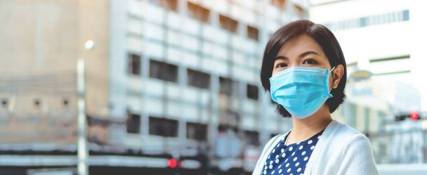 confident Young Beautiful Asian woman looking at camera wearing blue protective face mask for prevent pandemic virus, air pollution, covid-19 or coronavirus at outdoor, Banner - Фото, зображення