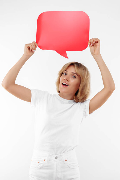 Cheerful young blonde woman holding red blank speech bubble over white background. - Valokuva, kuva