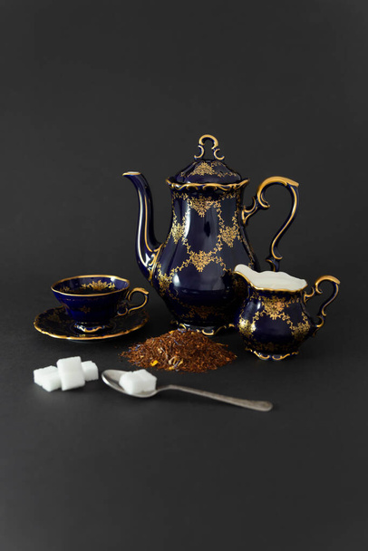 Still life with a beautiful cobalt blue colored vintage porcelain tea set, spoon with sugar cubes, milk jug and dry tea leaves. - Foto, Imagen
