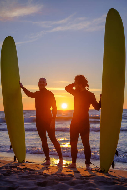 Άντρες surfers στέκεται κοντά κυματίζει θάλασσα το βράδυ - Φωτογραφία, εικόνα