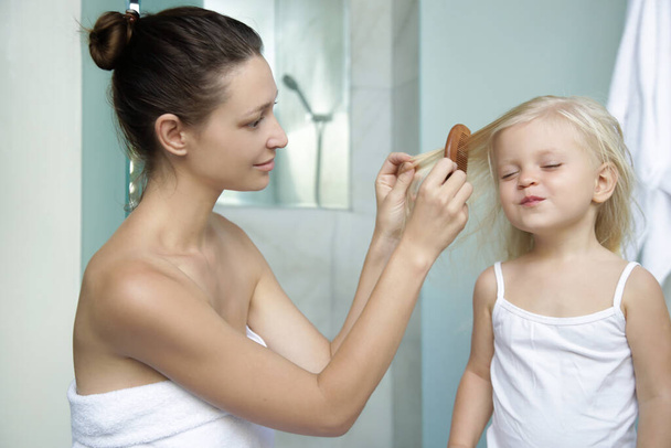 Anya fésüli a kislánya haját a fürdőszobában.  - Fotó, kép