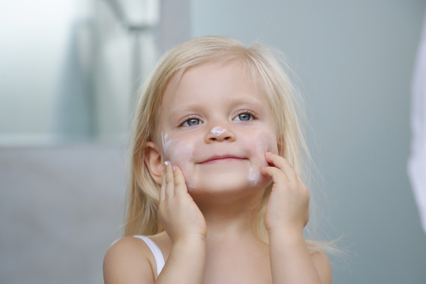 Чарівна блондинка кавказька дівчинка наносить крем на її обличчя
  - Фото, зображення