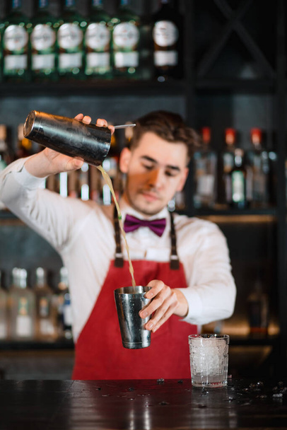 Barman pouring fresh cocktail from shaker into the glass on the bar counter - Photo, image