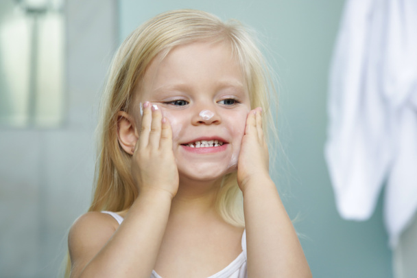 Adorable blonde caucasian toddler girl applying cream on her face  - Φωτογραφία, εικόνα