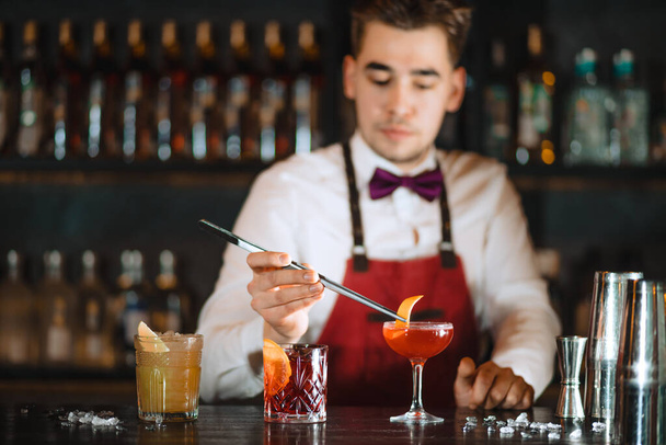 Bartender adding to cocktail orange zest with tweezers on the bar counter - Fotoğraf, Görsel