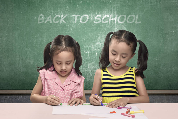 Asian little girl with a crayon drawing in the paper on the table. Back to School concept - Φωτογραφία, εικόνα