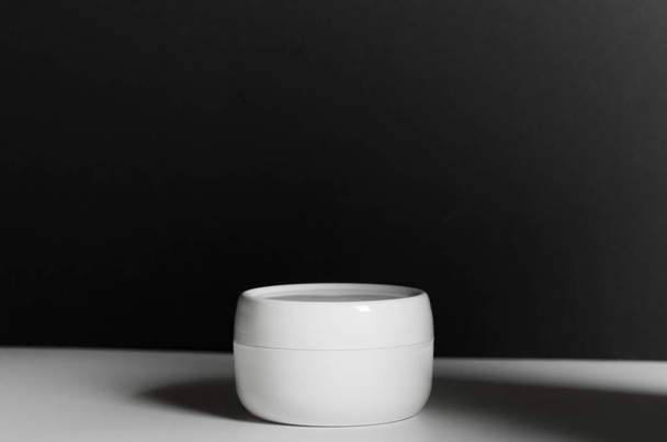 Closed white jar of face cream on a black background with dark shadow. Cosmetic moisturizing product - Фото, зображення