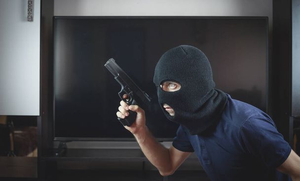Killer with a pistol and black balaclava in home. - Photo, Image
