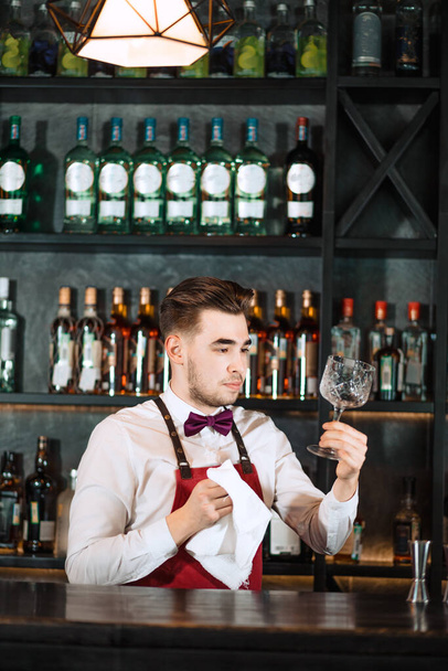 Bartender standing at bar counter, cleaning glasses with towel - Фото, зображення