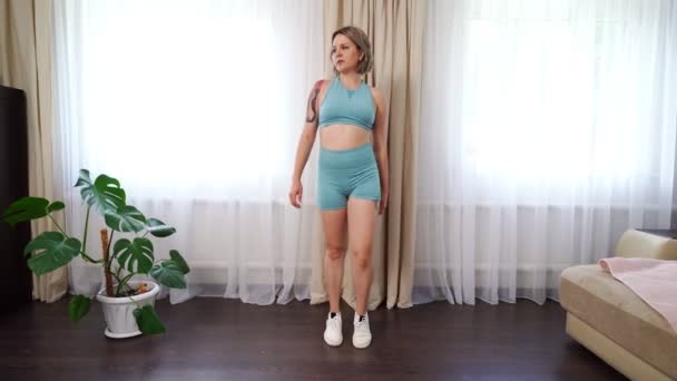 girl with tattoo in blue tracksuit sports at home, walking on spot - Metraje, vídeo