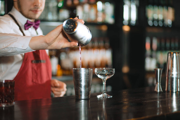 Barman pouring fresh cocktail from shaker into the glass on the bar counter - Foto, afbeelding