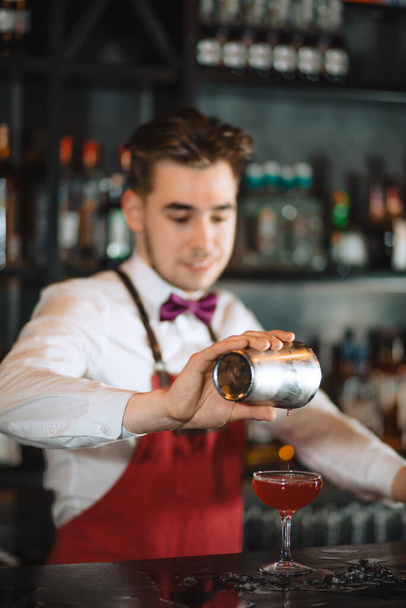 Barman pouring fresh cocktail from shaker into the glass on the bar counter - Foto, Bild