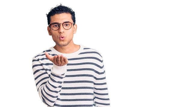 Hispanic handsome young man wearing casual clothes and glasses looking at the camera blowing a kiss with hand on air being lovely and sexy. love expression.  - Foto, Bild