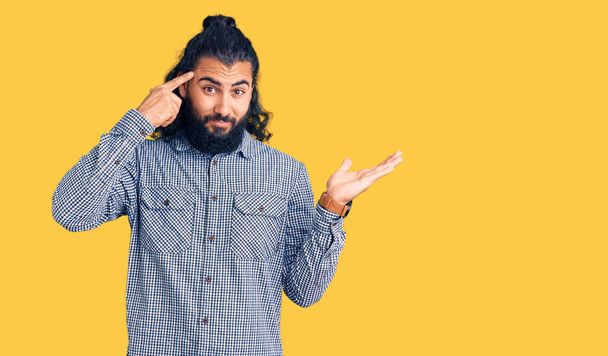 Homem árabe jovem vestindo roupas casuais confuso e irritado com a palma aberta mostrando espaço de cópia e apontando o dedo para a testa. Pense nisso..  - Foto, Imagem