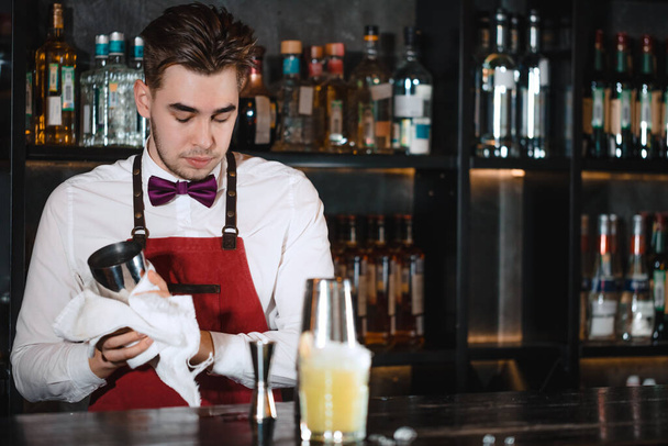Bartender standing at bar counter, cleaning glasses with towel - Photo, image