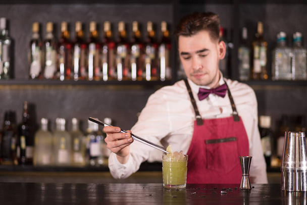 Barman finishing cocktail decorating it with a slice of lime using tweezers. - Zdjęcie, obraz