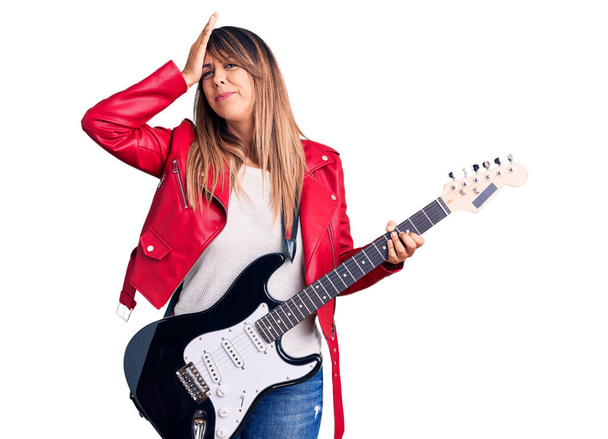 Young beautiful woman playing electric guitar stressed and frustrated with hand on head, surprised and angry face  - Fotoğraf, Görsel