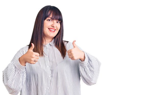 Young plus size woman wearing casual clothes success sign doing positive gesture with hand, thumbs up smiling and happy. cheerful expression and winner gesture.  - Photo, Image