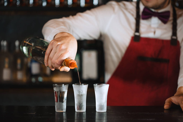 Hands of bartender pouring some drink into shot glasses on a wooden counter - Фото, изображение