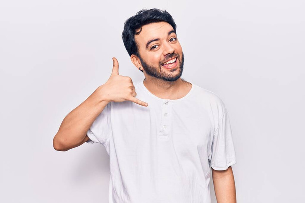 Young hispanic man wearing casual clothes smiling doing phone gesture with hand and fingers like talking on the telephone. communicating concepts.  - Фото, изображение