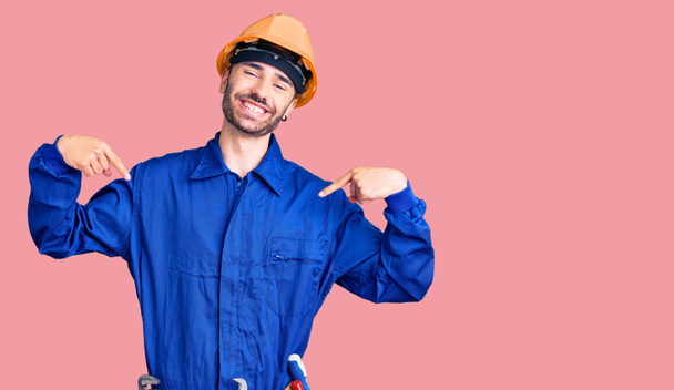 Joven hombre hispano vistiendo uniforme de trabajador que mira confiado con sonrisa en la cara, señalándose con los dedos orgullosos y felices
.  - Foto, imagen