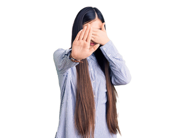 Mladá krásná Číňanka nosí ležérní košili zakrývající oči rukama a dělá stop gesto se smutným a ustrašeným výrazem. trapný a negativní koncept.  - Fotografie, Obrázek